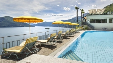 Piscine avec des parasols jaunes et des chaises longues, donnant sur un lac et des montagnes à l'arrière-plan.