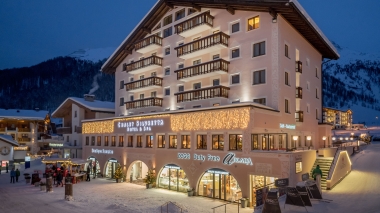 An illuminated alpine-style hotel in the snow at night.