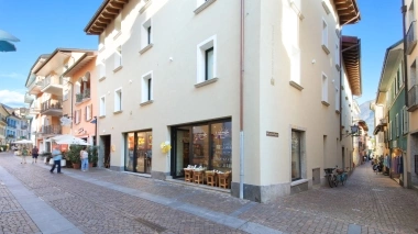 A quiet cobblestone street with multi-story buildings and shops under a blue sky.