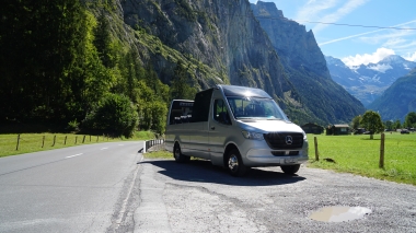 Ein silberner Transporter steht auf einer Landstrasse vor einer beeindruckenden Bergkulisse.