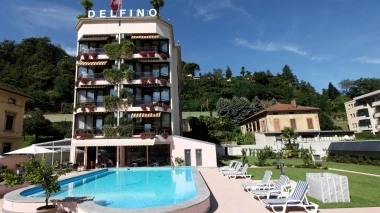 Hotel con piscina, circondato da lettini prendisole e giardino, davanti a una collina boscosa.