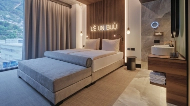 Chambre d'hôtel moderne avec un grand lit, des panneaux muraux en bois et une salle de bain ouverte.