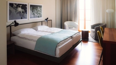 A modern hotel room with a double bed, two armchairs, and a desk.