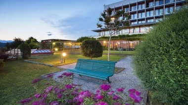 A green park bench in the garden in front of a multi-story building at dusk.