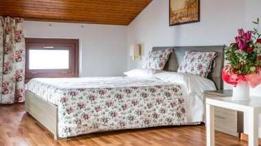 Chambre confortable avec plafond en pente, literie fleurie et bouquet de fleurs sur la table.