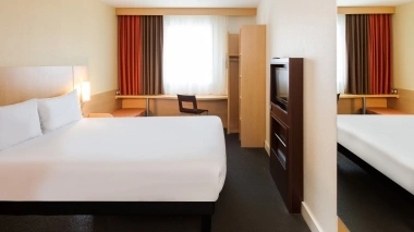 A simply furnished hotel room with a large bed, a desk, a chair, and curtains.