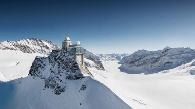 A research station on a snow-covered mountain peak under a blue sky.