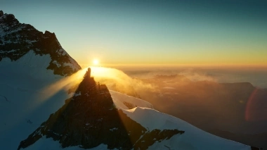 Coucher de soleil derrière un sommet de montagne enneigé avec du brouillard.