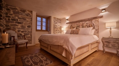 Cozy bedroom with wooden floor, a large bed, and natural stone walls.