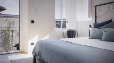 Modern bedroom with a large bed, blue coverlet, balcony, and plenty of natural light.