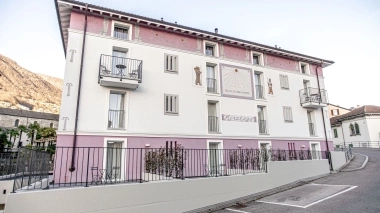 Multistory building with white and pink walls, balconies, and murals; mountains in the background.