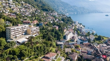 Una città collinare con edifici circondati da alberi e un grande lago sullo sfondo.