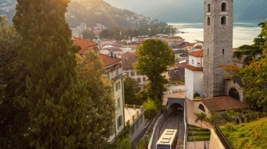 Una vista della città all'alba con montagne, un campanile e una ferrovia di montagna.