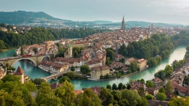 A city view of Bern, Switzerland, with the river Aare, historical buildings, and a large church in the background.