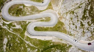 Luftaufnahme einer Serpentinenstrasse in bergiger Landschaft mit zwei Autos.