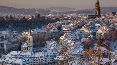 Un paesaggio urbano innevato con edifici storici e una grande chiesa sullo sfondo.
