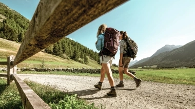 Two people hiking on a gravel path through a green landscape with mountains in the background.