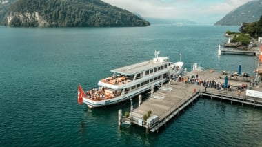 A ship is docked at a pier, surrounded by green hills and blue water.