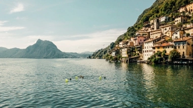 Eine hübsche Seelandschaft mit Häusern am Hang und einem Berg im Hintergrund.