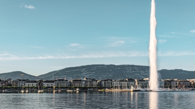 A large water fountain rises in front of a skyline with mountains in the background.