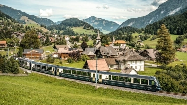 Eine idyllische Berglandschaft mit einem Zug, der durch ein malerisches Dorf fährt.