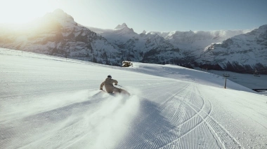 Un skieur sur une piste fraîchement damée avec des montagnes enneigées en arrière-plan.