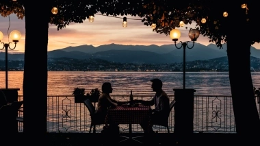 Two people sitting at a table by the lakeside at sunset.