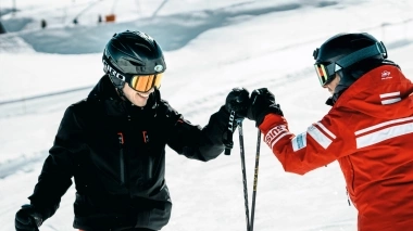 Two skiers on a ski slope high-fiving each other.