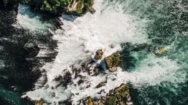 Aerial view of a large waterfall with rocks and a yellow boat on the water.