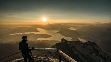 Una persona sta su una montagna, guardando un lago e il paesaggio circostante all'alba.