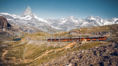 Un treno rosso attraversa il paesaggio montano davanti al Cervino.