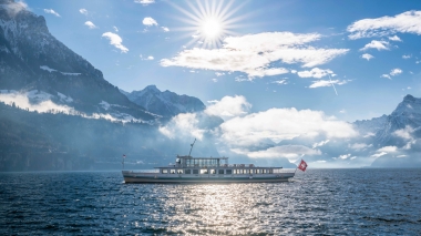 Ein Schiff auf einem See, umgeben von Bergen unter strahlender Sonne.