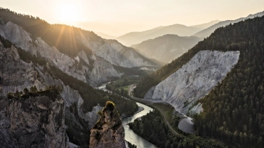 Tramonto su una gola di montagna con un fiume e pendii alberati.