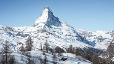 A snowy mountain landscape with a prominent peak in the background and an empty chairlift in the foreground.