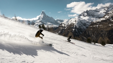 Two skiers on a snowy slope with the Matterhorn in the background.