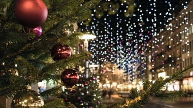 Christmas tree with red ornaments, with the glowing lights of a city street in the background.