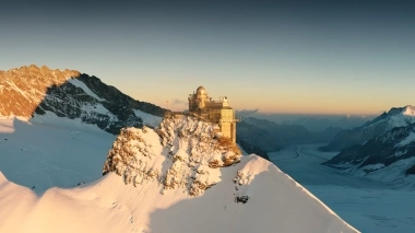 Observatorium auf verschneitem Berggipfel bei Sonnenuntergang.