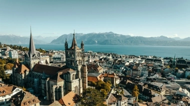 Vue aérienne d'une église historique dans une ville avec un lac et des montagnes à l'arrière-plan.