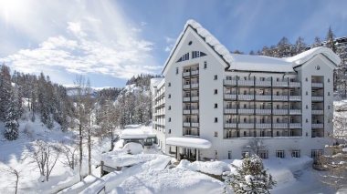 A snowy hotel building in the mountains under a clear sky.