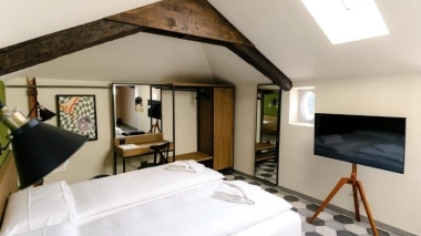 Chambre mansardée avec poutres en bois, lit double, télévision à écran plat, bureau et miroir.