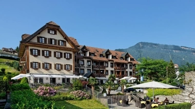 Traditional hotel building with garden and mountains in the background.