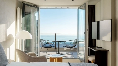 Une chambre d'hôtel moderne avec vue sur le lac, deux chaises et une table sur le balcon.