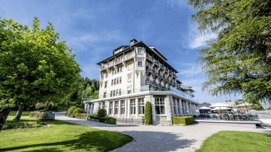 Historic building with large windows, surrounded by trees and well-kept lawn under a clear blue sky.