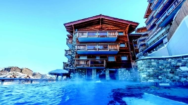 A wooden cabin by the edge of a pool with mountains in the background.