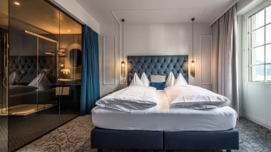 Luxurious hotel room with a modern double bed, stylish lighting, and a large window.