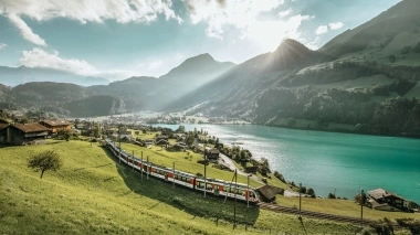 An idyllic mountain landscape with a train passing by a lake.