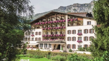 Garden and house of Hotel Adula with mountains in the background