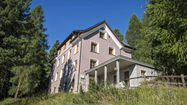 A building in front of a meadow and surrounded by trees