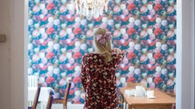 A woman stands in front of a wall painted with flowers.