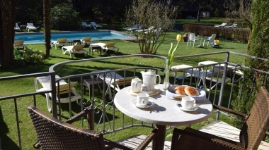 Balcony overlooking a garden with a pool and sun loungers.